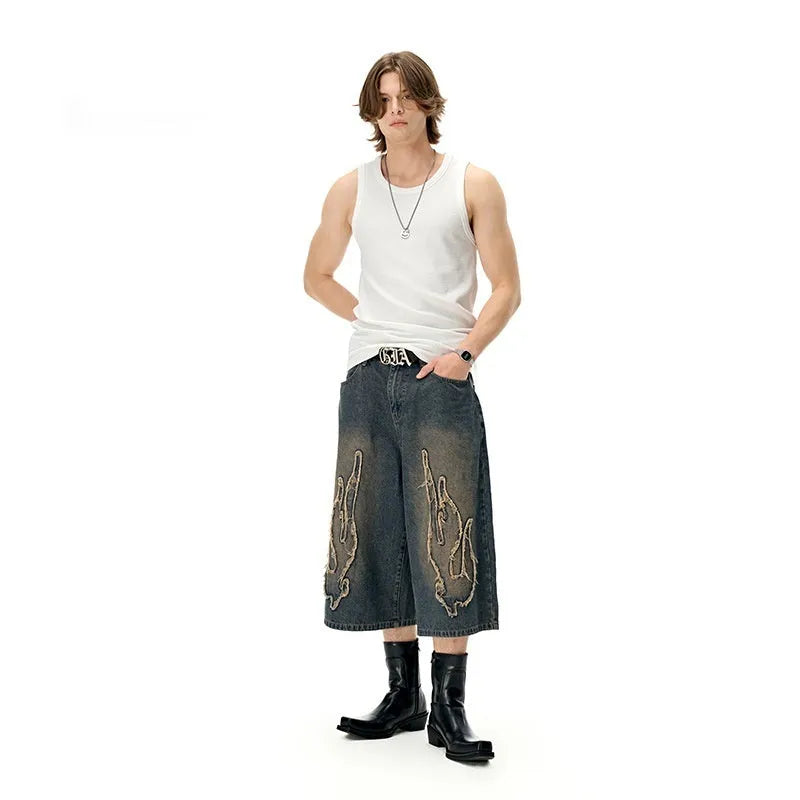 Men's black denim cropped shorts with red and yellow flame patch embroidery on the leg.