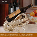 Rose gold resin lobster ornament holding a wine bottle on a wooden shelf.