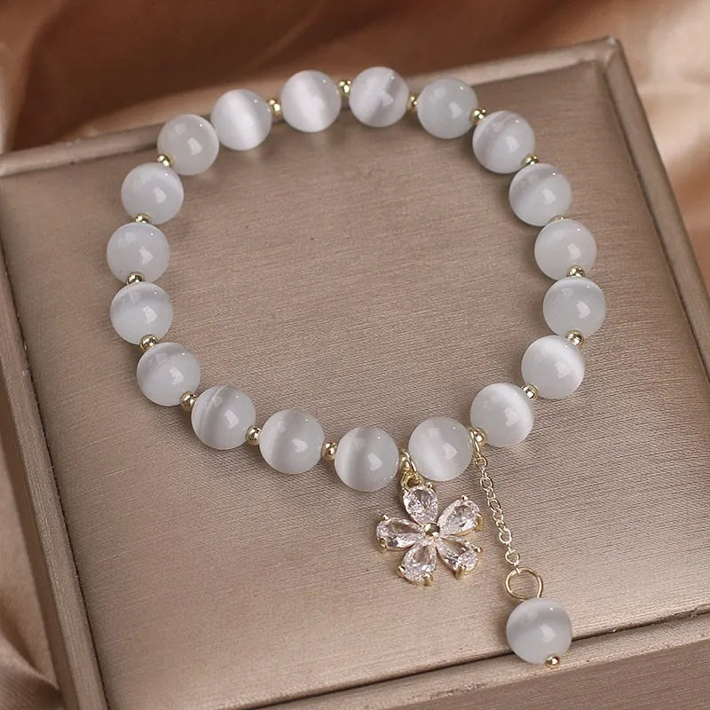 White cat's eye stone flower bracelet with silver-tone details and a hanging tassel charm.