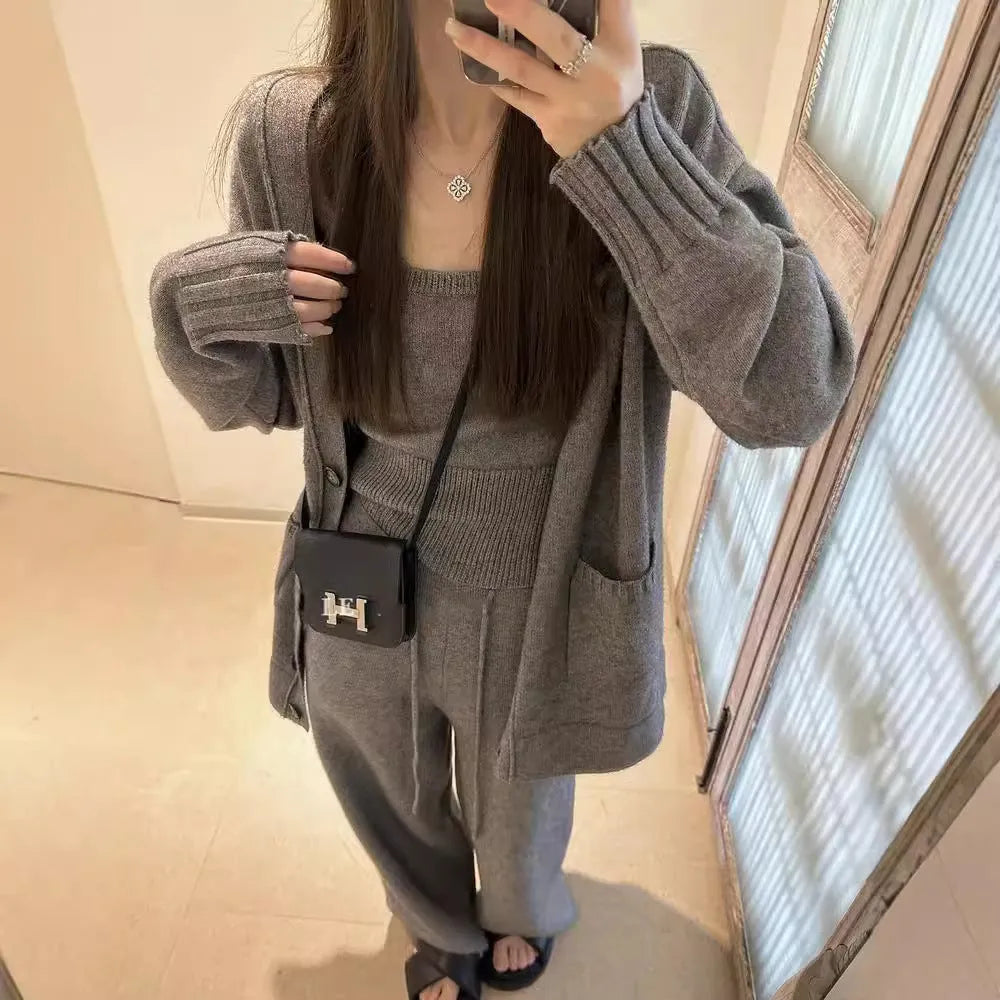 Women's beige knitted cardigan three-piece set with sleeveless vest and suspender trousers on a hanger.