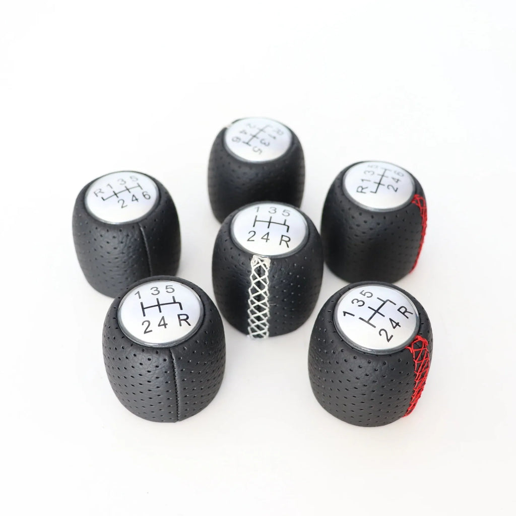 Sewn wrapped black perforated leather gear shift handball for Alpha vehicles on a silver cover.