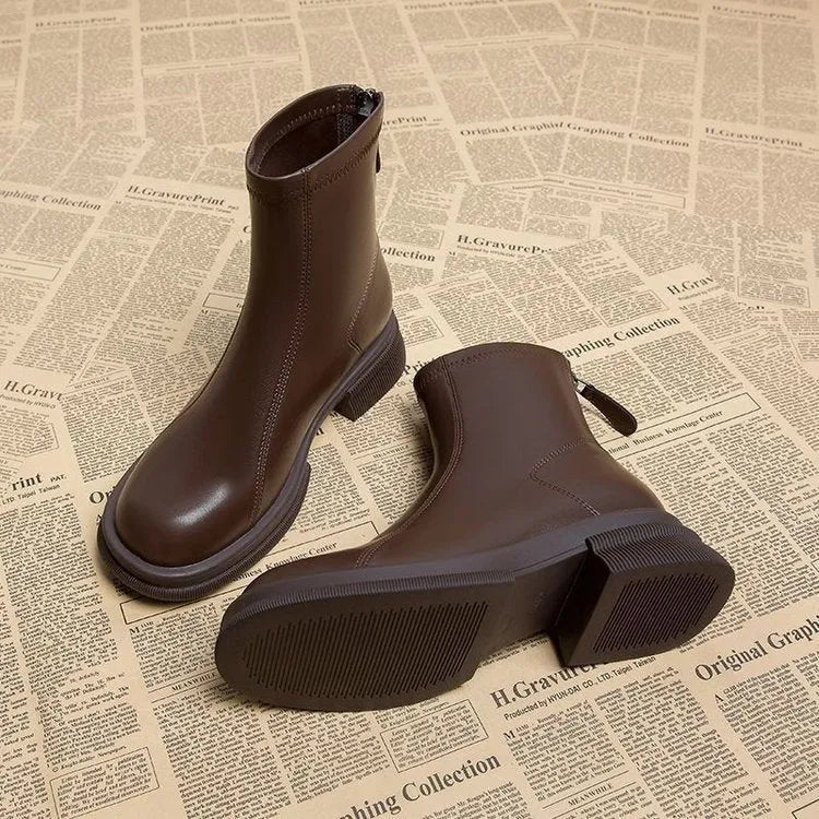 Women's black ankle boot with flat heel, round toe, and back zip on a plain background.