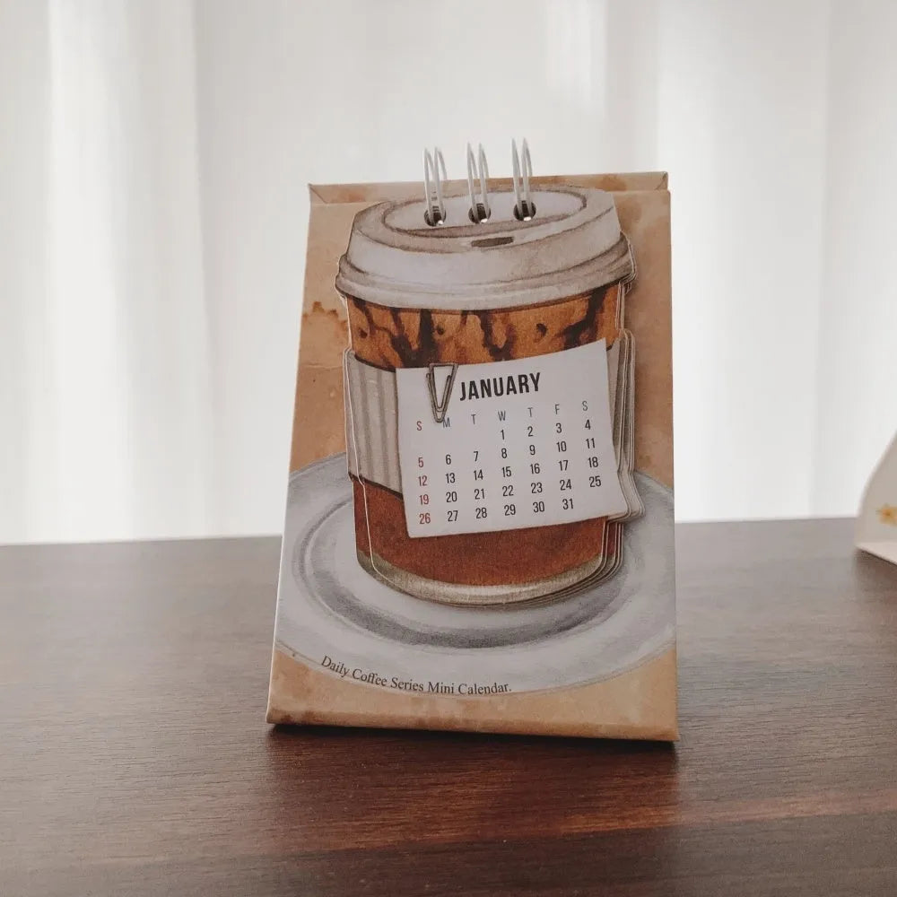 Mini A6 paper desk calendar for 2025 open to a monthly page with coffee-themed design.