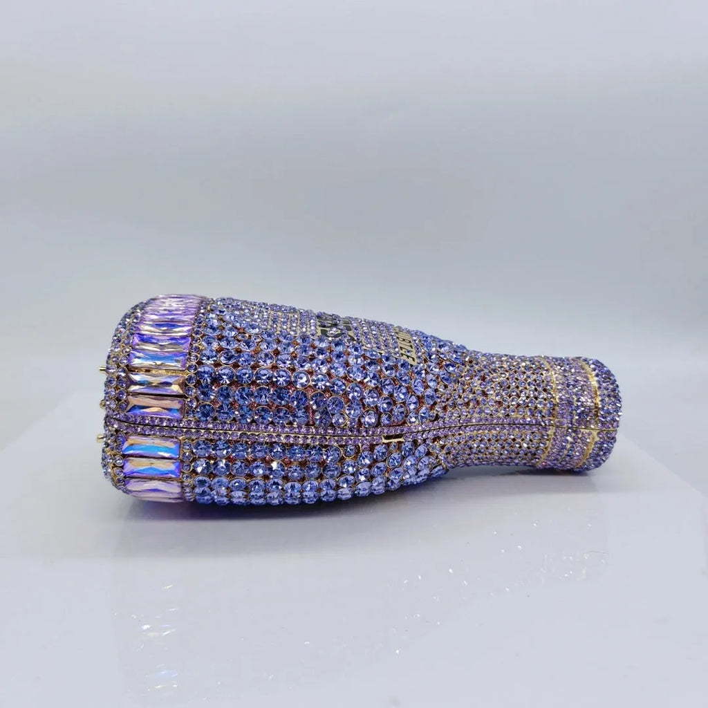 Gold hard-shell champagne bottle shaped evening clutch with rhinestones on a table.