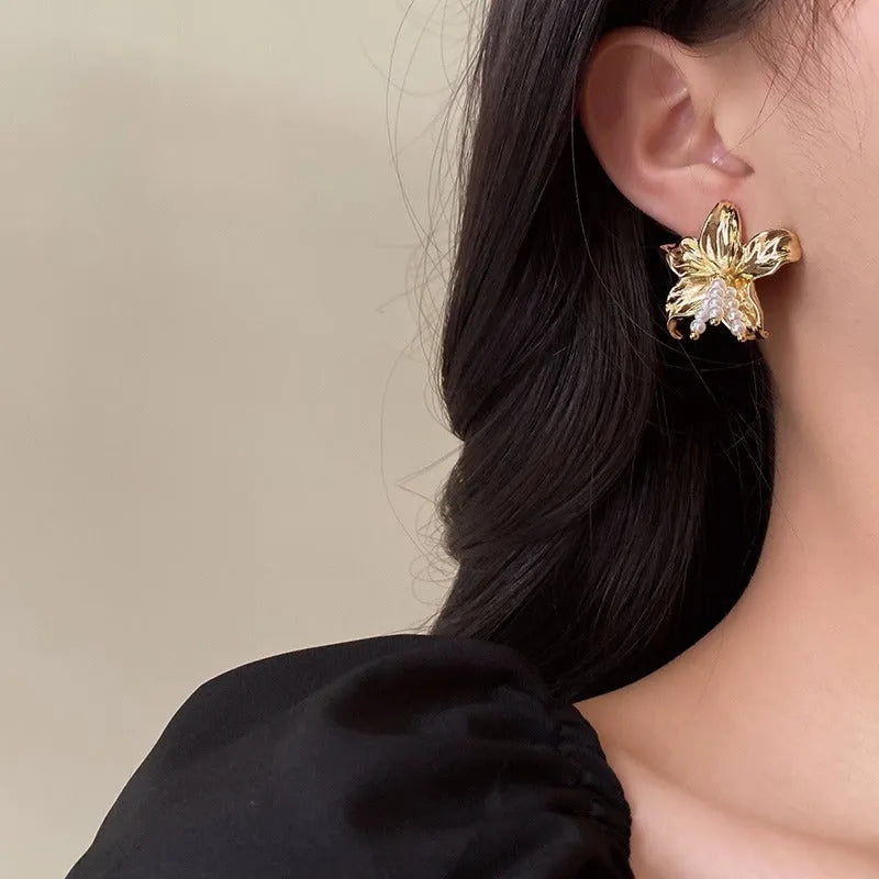 A pair of exaggerated gold metal flower earrings with pearls, showing niche style design.