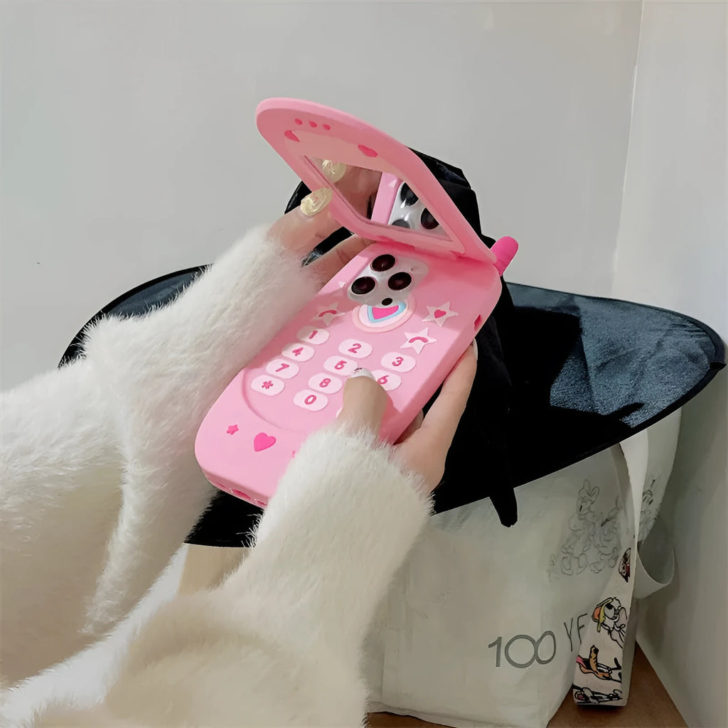 Pink silicone flip phone-shaped iPhone case with a built-in mirror and cute cartoon design.
