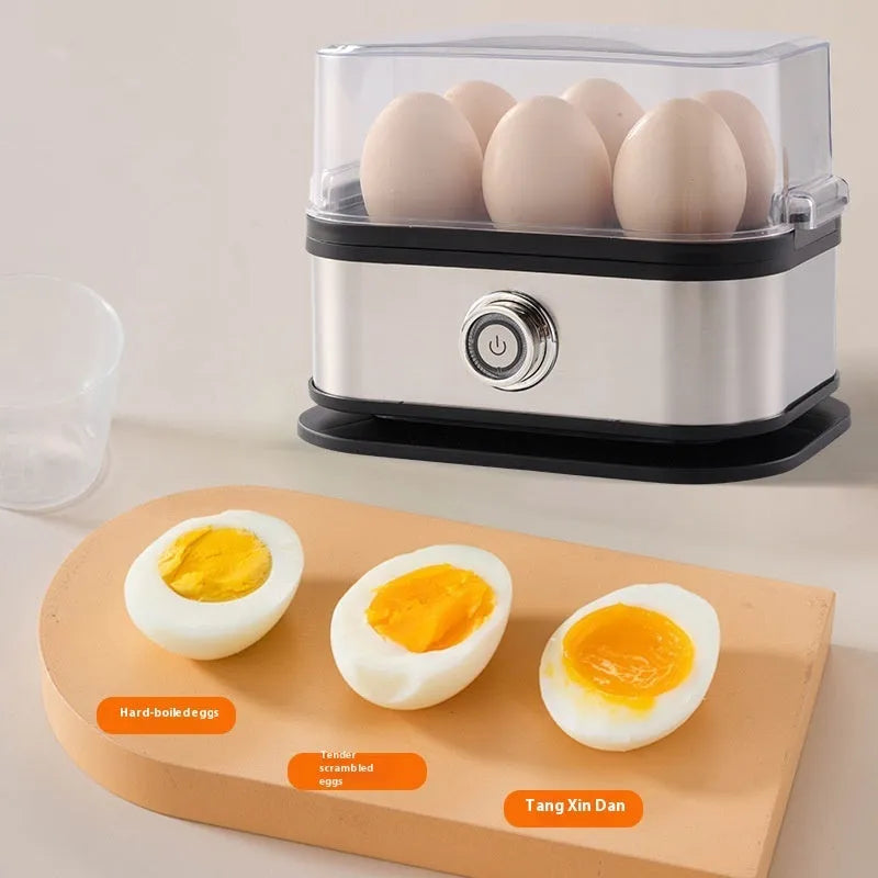 Small black stainless steel portable egg boiler with plug adapters on a countertop.